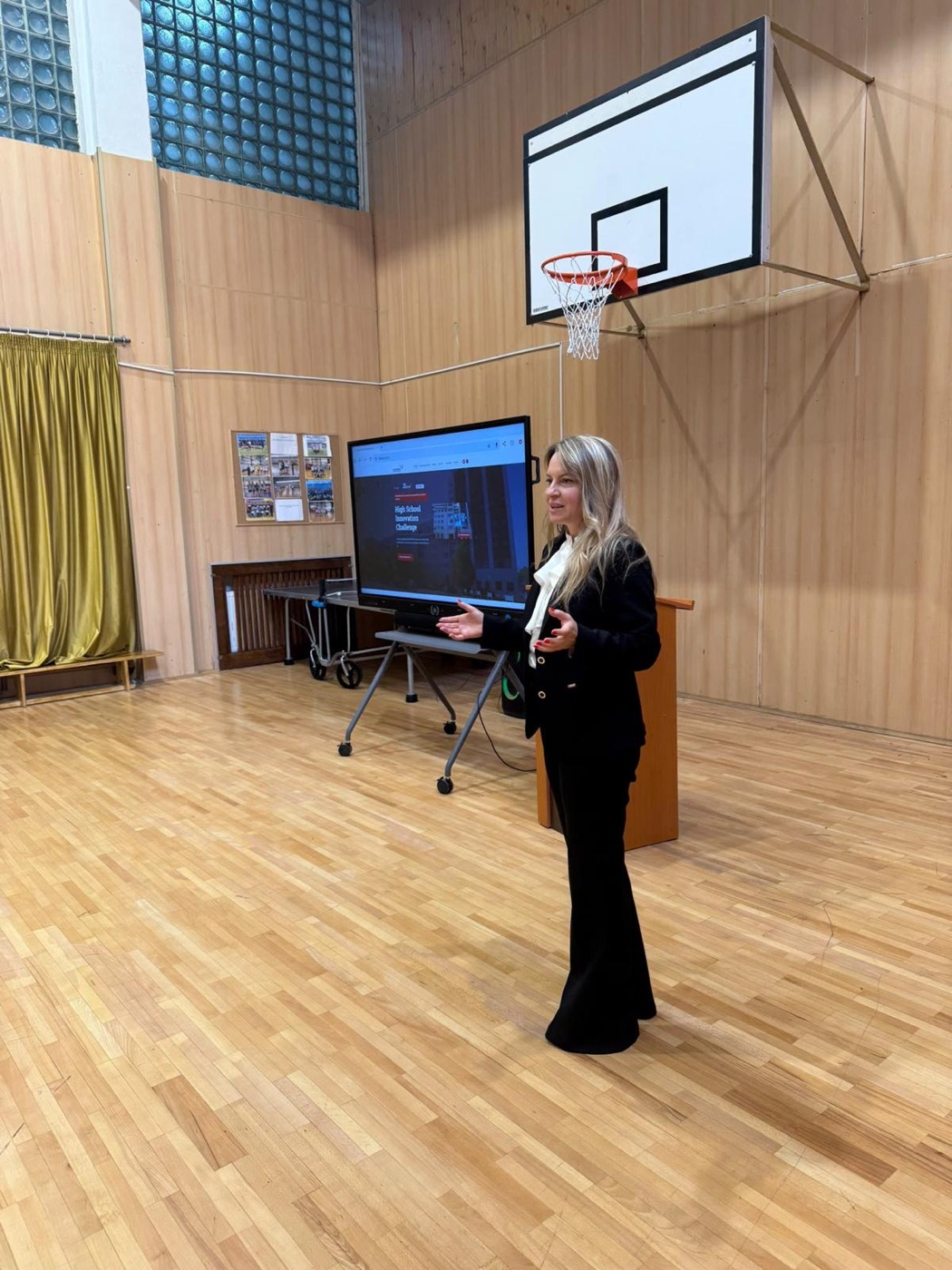 Adina Zara presenting the High School Innovation Challenge in a high-school gym